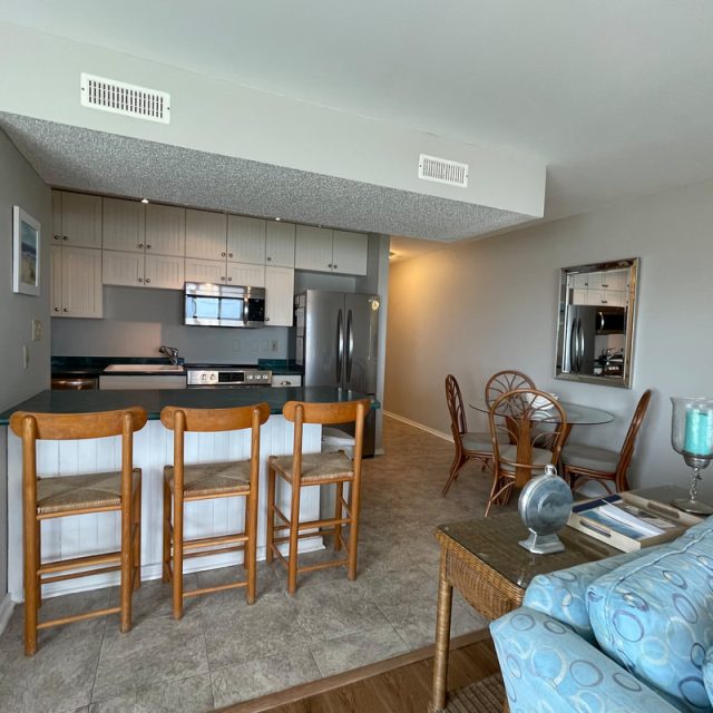Open kitchen and dining area with wooden barstools, glass table, and light-colored furnishings in a modern apartment.