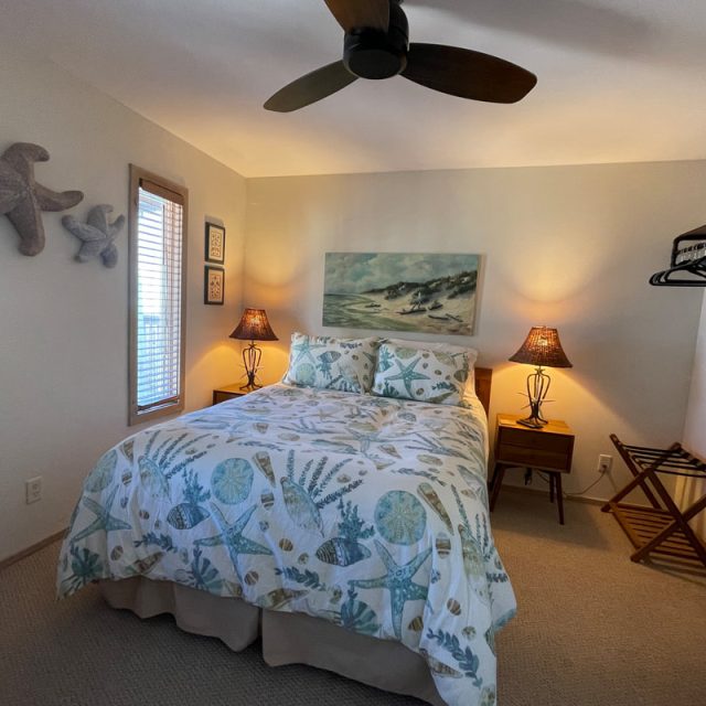 Bedroom with a double bed, ocean-themed bedding, nightstands, lamps, ceiling fan, and wall art.