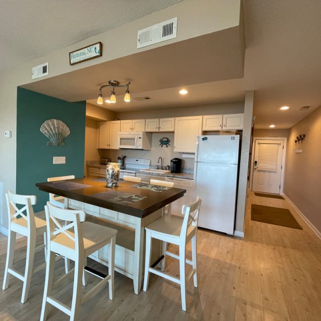 Small kitchen with white cabinets, an island with four chairs, and teal accent wall in a modern apartment.
