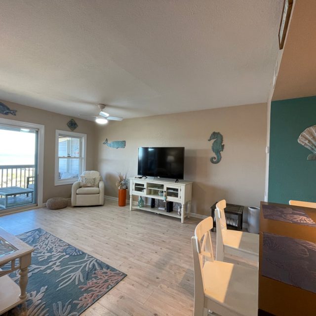 Living room with beach decor, a TV, glass doors to a balcony, and dining area with turquoise accent wall.