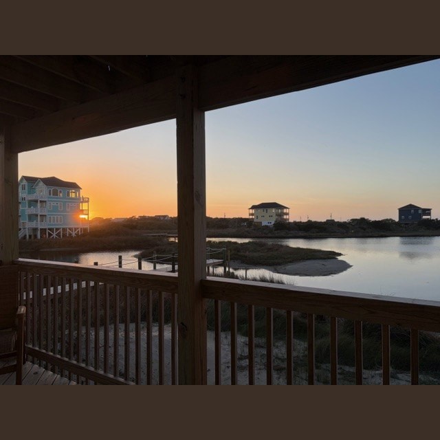 View of houses by water at sunset, seen from a wooden porch with railings and shadows cast by the setting sun.