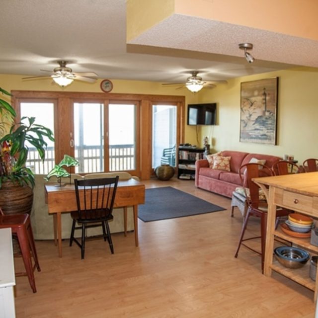 Open-plan living and dining area with yellow walls, wooden floors, and large windows leading to a balcony.