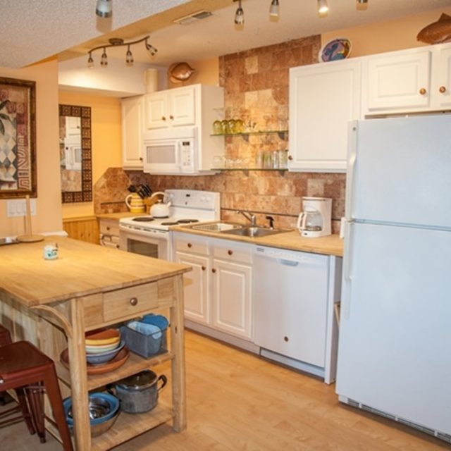 Cozy kitchen with white cabinets, wood countertops, island with stools, and various appliances and dishes.