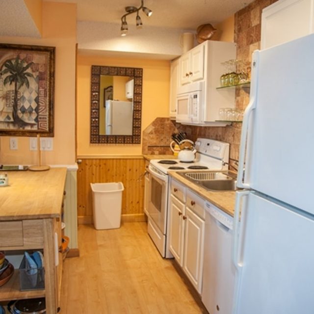 Small kitchen with white cabinets, a white fridge and stove, wood island, and a wall mirror above a trash can.