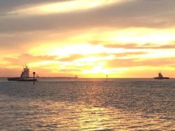 Two boats on calm water at sunset with a bright, golden sky and clouds in the background.