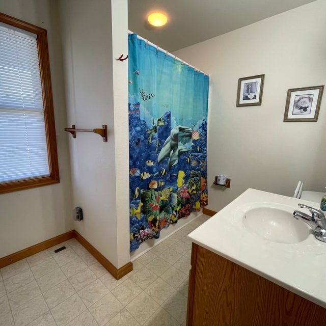 Bathroom with a sink, ocean-themed shower curtain, framed pictures, window with blinds, and towel rack on the wall.