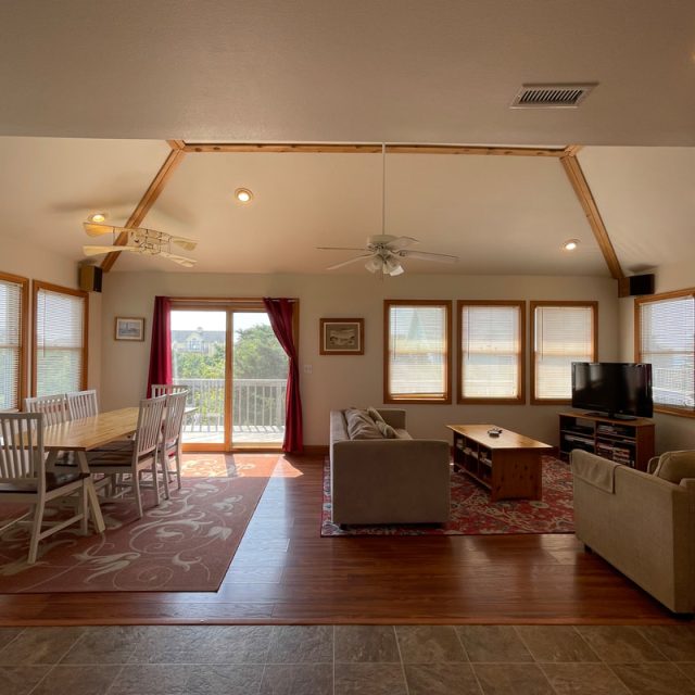 Open living room and dining area with large windows, a couch, TV, dining table, and sliding glass door to a balcony.
