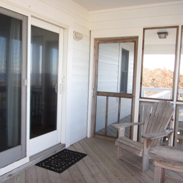 Wooden deck with two chairs, a small table, sliding glass door, and a screened door attached to a white house.