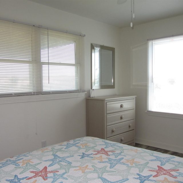 Bedroom with two windows, a dresser with a mirror, and a bed with a starfish-patterned bedspread.