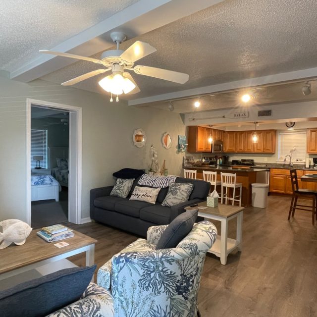 Living room with two sofas, a ceiling fan, and a view into the kitchen and a bedroom in the background.