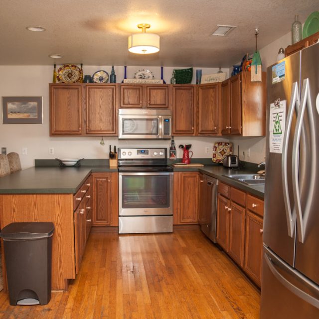 Modern kitchen with wooden cabinets, stainless steel appliances, island seating, and hardwood floors.
