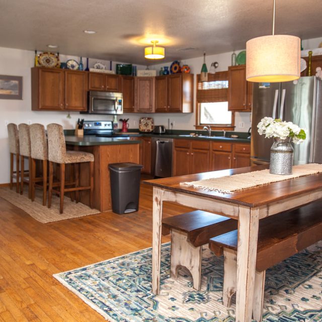 Open kitchen with wooden cabinets, stainless steel appliances, a dining table with benches, and a floral centerpiece.