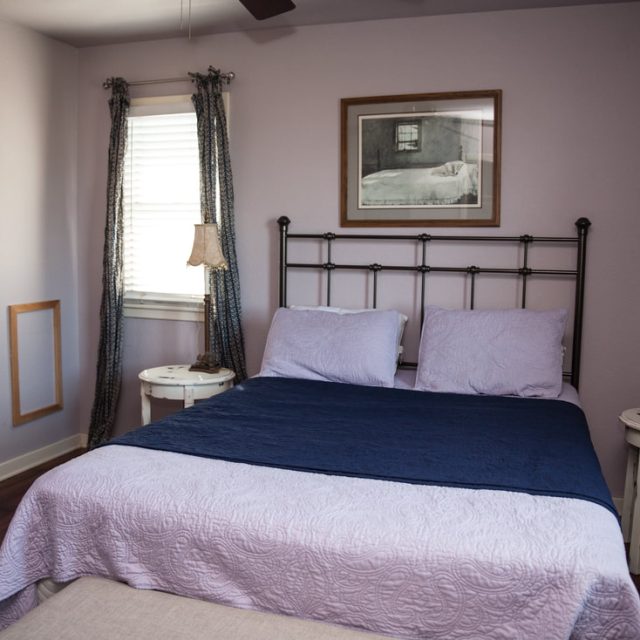 A neatly made bed with blue and white linens sits between two round nightstands in a softly lit bedroom.