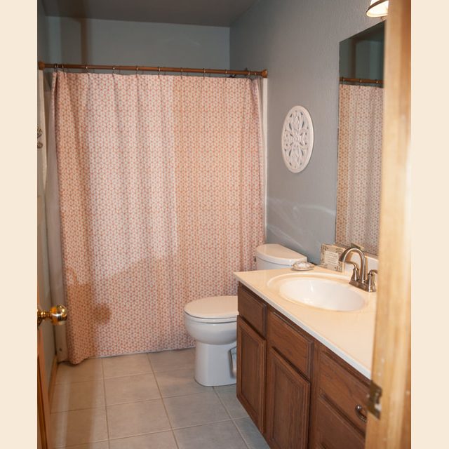 Small bathroom with a shower curtain, toilet, wooden vanity, sink, mirror, and tile floor.