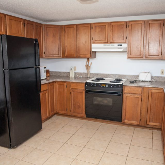 Kitchen with wood cabinets, black fridge and stove, beige countertops, sink, and tiled floor.
