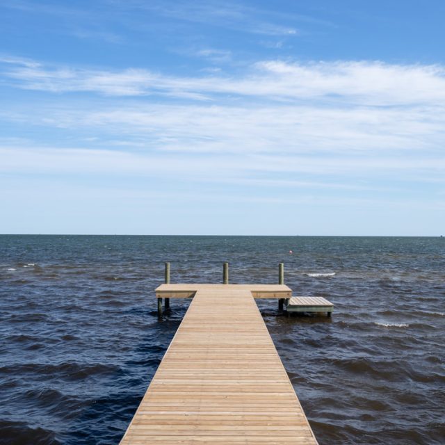 Wooden dock extends over choppy water under a blue sky with scattered clouds.