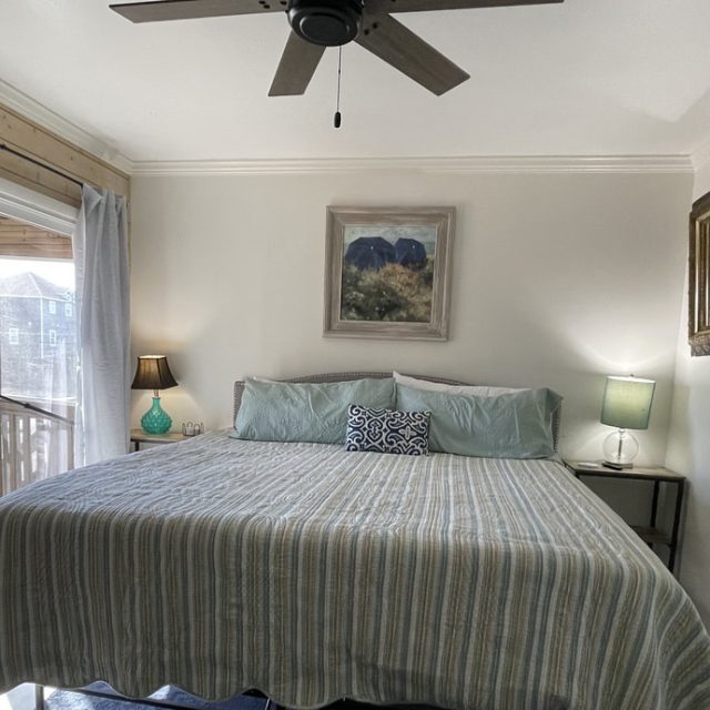 Bedroom with a king bed, striped bedding, two bedside tables with lamps, ceiling fan, and wall art above the bed.