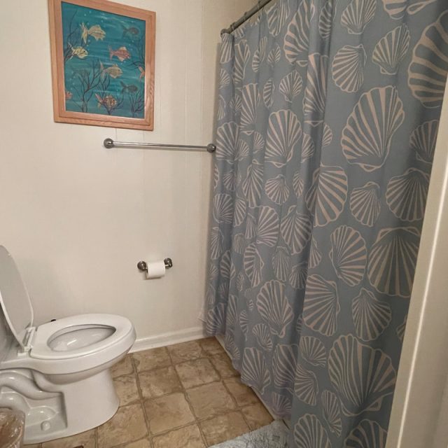 A bathroom with a toilet, sea-themed shower curtain, ocean art on the wall, and tile floor.