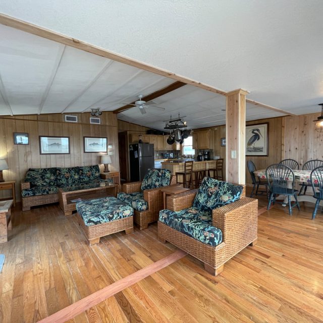 Open-plan living and dining area with wood paneling, wicker furniture, floral upholstery, and hardwood floors.
