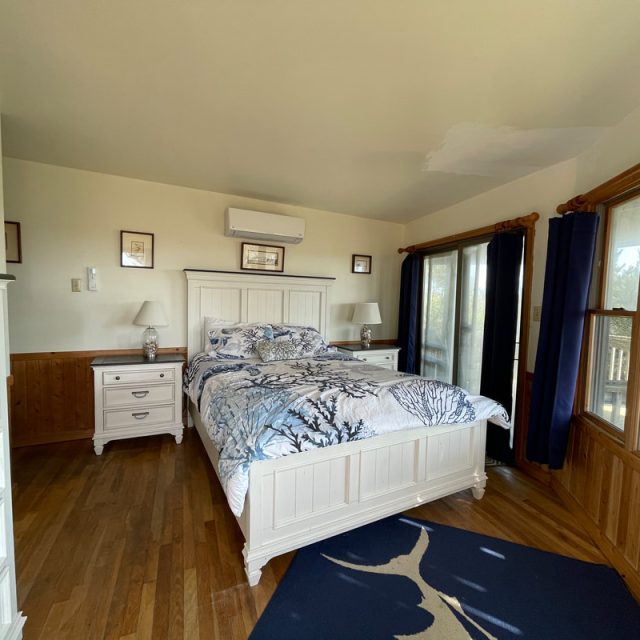 Bedroom with white furniture, double bed, nightstands, dresser, large windows, and hardwood floor.