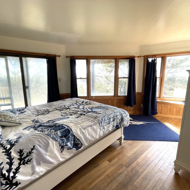 Bright bedroom with large windows, wooden floors, a bed with blue floral bedding, and dark blue curtains.