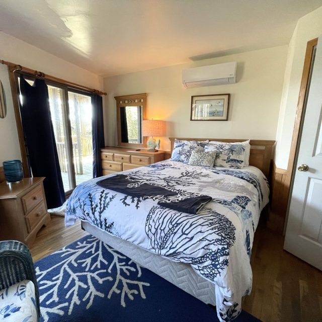 Bedroom with a double bed, dresser, mirror, and sliding glass doors leading to a deck, decorated in a coastal theme.