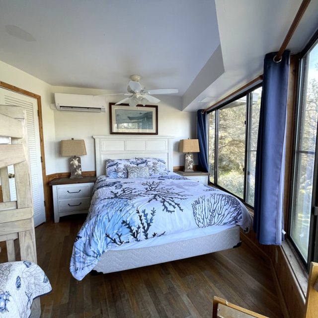 Bedroom with a double bed, bunk bed, large windows, wooden floor, and nature view outside.
