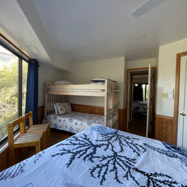 Bedroom with a bunk bed, double bed, wooden bench by the window, and a door leading to another room.