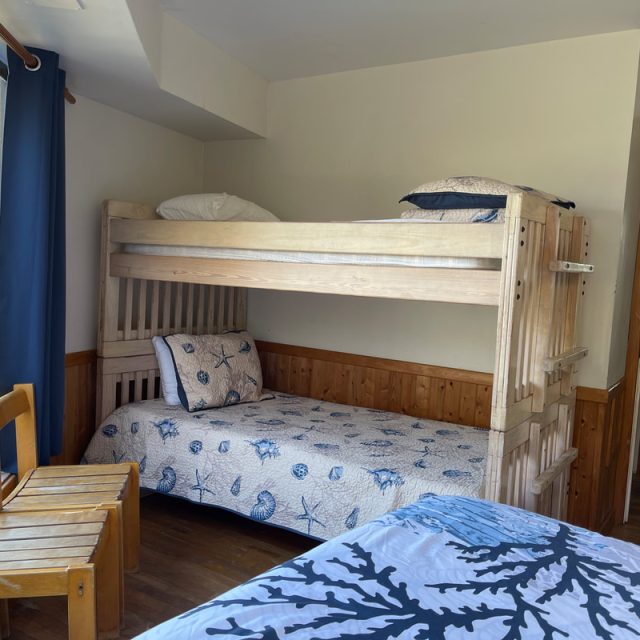 A bedroom with wooden bunk beds, a small wooden chair, and a bed with blue and white ocean-themed bedding.