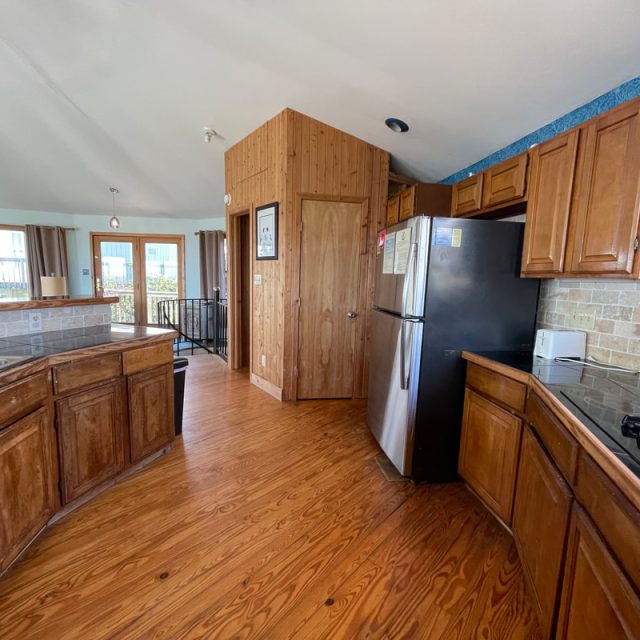 Kitchen with wood cabinets and floors, stainless steel fridge, stove, and large windows letting in natural light.