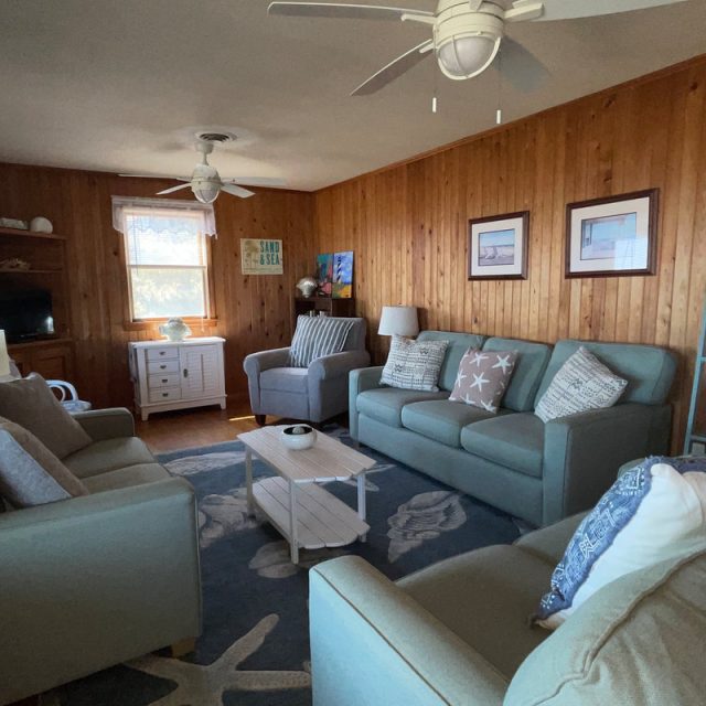 Cozy living room with wooden walls, three sofas, a rug, a coffee table, and nautical-themed decor.