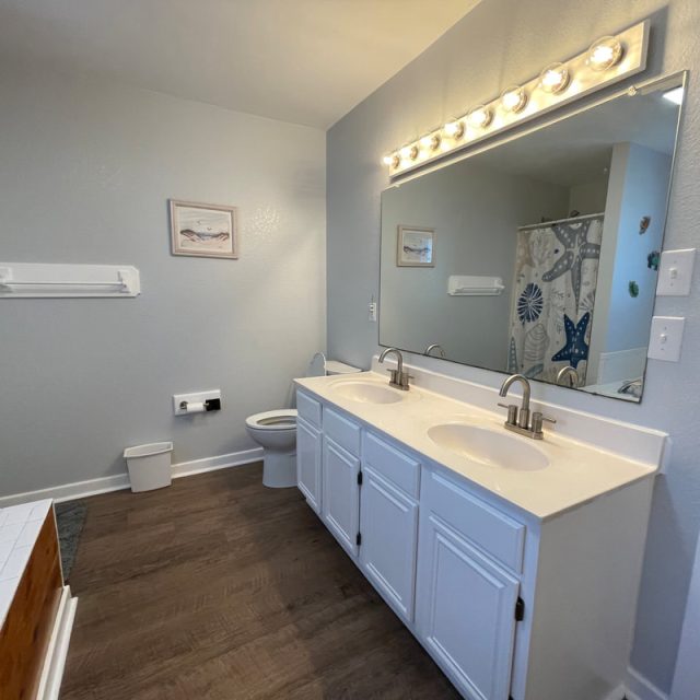 Bathroom with double sinks, large mirror, toilet, towel rack, and shower curtain with blue patterns.