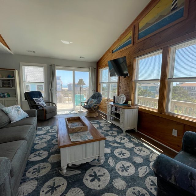 A sunlit living room with beach decor, blue furniture, large windows, and a glass door leading to a balcony.
