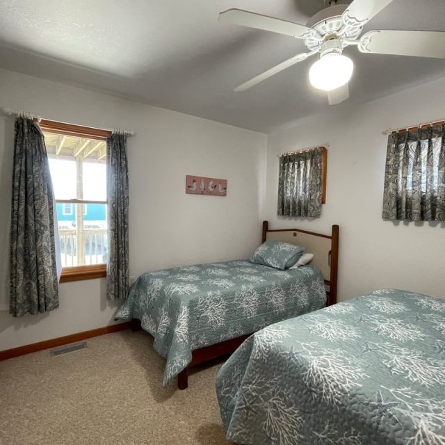 Bedroom with two twin beds, patterned bedding, ceiling fan, window, closet, and light-colored walls.