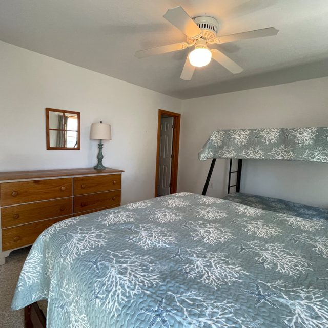 Bedroom with bunk beds, double bed, dresser with lamp, wall mirror, ceiling fan, and closed door.