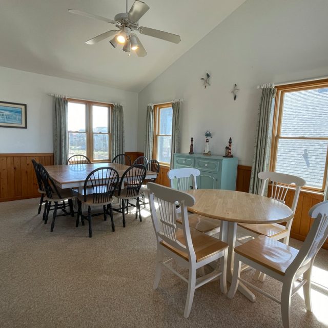 Dining room with two tables, chairs, a ceiling fan, large windows, and a light blue cabinet along the wall.