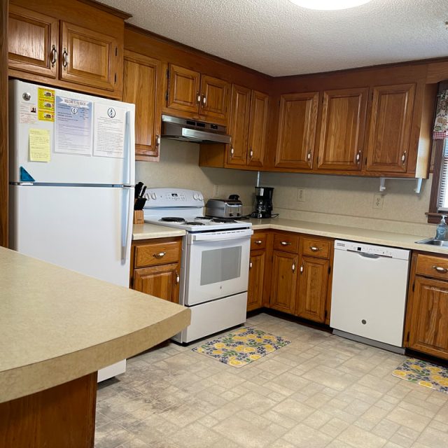 Kitchen with wooden cabinets, white appliances, beige counters, and floral mats on a light patterned floor.