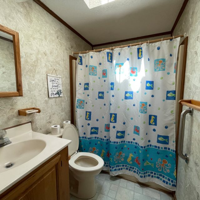 Small bathroom with a sink, toilet, wooden accents, and a shower with a colorful ocean-themed curtain.