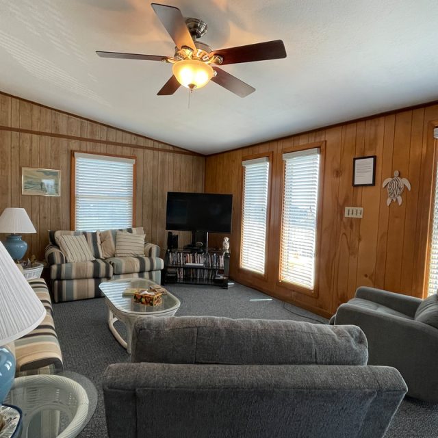 Wood-paneled living room with sofas, recliner, coffee table, TV, and windows with blinds letting in natural light.