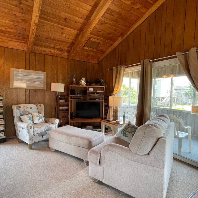 Living room with wood-paneled walls, armchair, ottoman, sofa, TV stand, and sliding glass door to a patio.