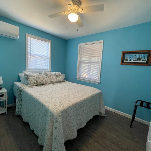 Bedroom with blue walls, a queen-size bed, two windows, a white dresser, and a ceiling fan.