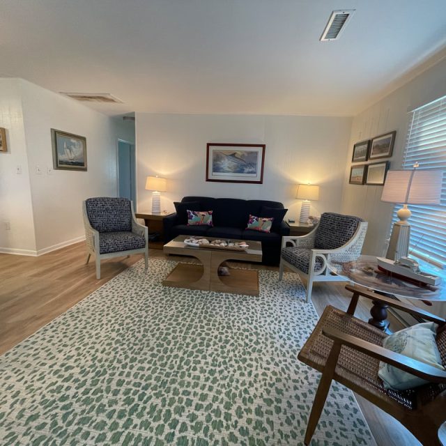 Living room with a dark sofa, four chairs, lamps, a coffee table, artwork, and large windows with blinds.