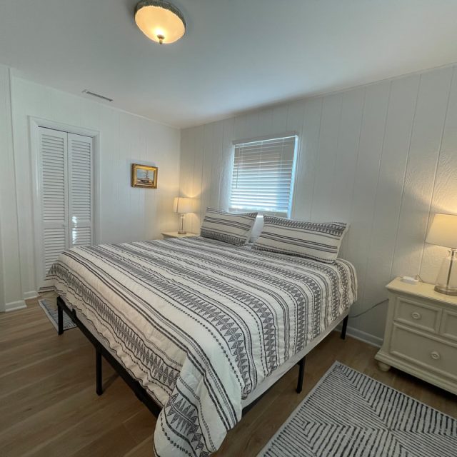 Bedroom with a striped bedspread, two nightstands with lamps, a rug, and a window with closed blinds.