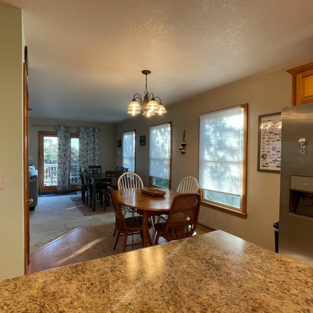 Kitchen and dining area with a round table, chairs, hanging light, windows, and stainless steel refrigerator.