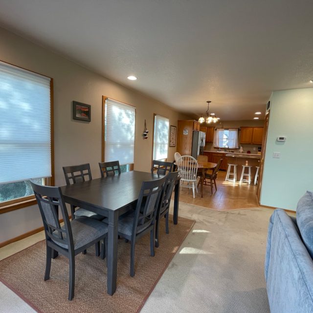 Dining area with a dark wood table and six chairs, adjacent to a kitchen with an island and barstools.