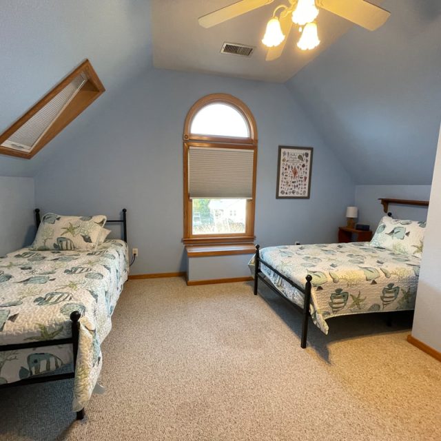 Bedroom with two twin beds, a window with shade, light blue walls, and a ceiling fan with lights.