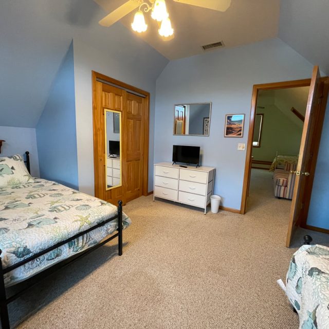 Bedroom with two twin beds, a dresser with a small TV, a closet, and an open door leading to another room.