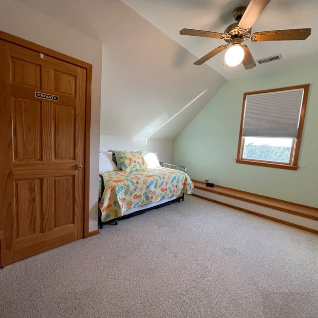 Bedroom with two twin beds, a ceiling fan, carpeted floor, window, and a door labeled “Private.”.