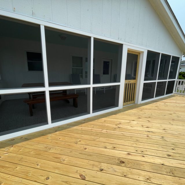 Wooden deck with a screened-in porch area attached to a white house; outdoor furniture visible through the screens.