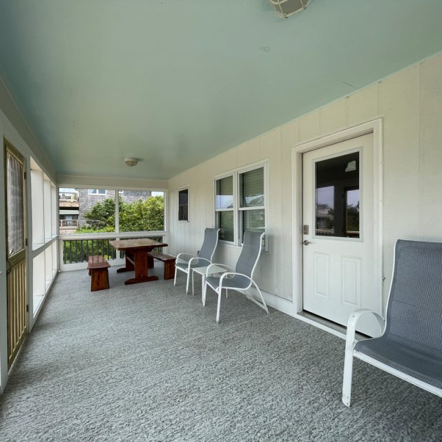 Screened porch with gray carpet, white chairs, a wooden table with benches, and light blue ceiling.